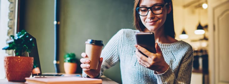 Mulher segurando copo de café e smartphone, sorrindo